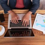 Person working on laptop with tablet and coffee