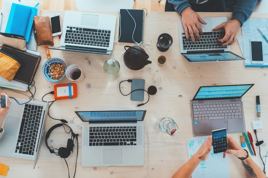 People working at a table with laptops and phones.